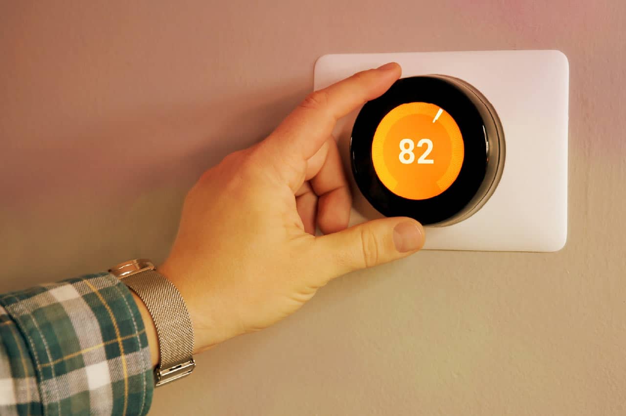 a hand turning up a thermostat to 82 degrees